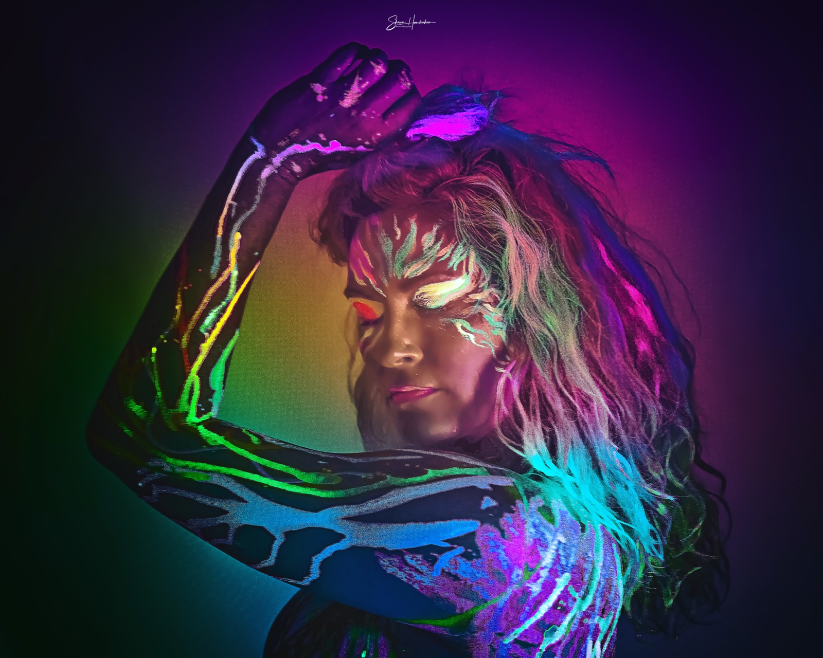 A figure in rainbow UV body and face paint, arms lifted, glowing under black light