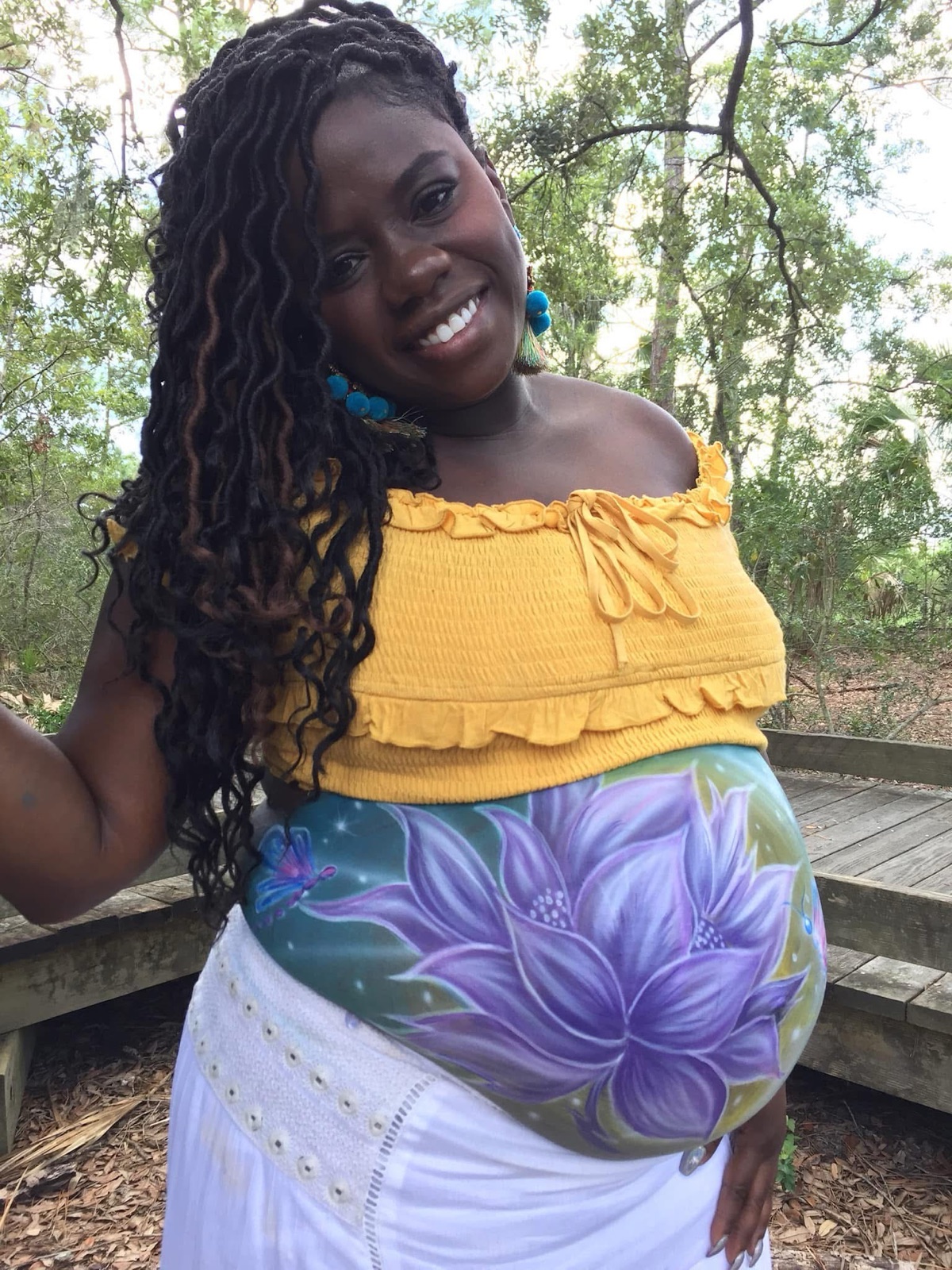A mother-to-be with a lotus painted across her belly, outdoors