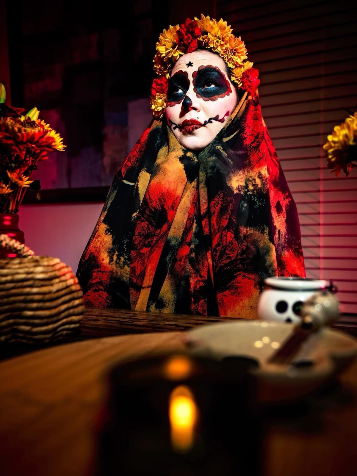 A sugar-skull face with a floral crown, lit by candlelight