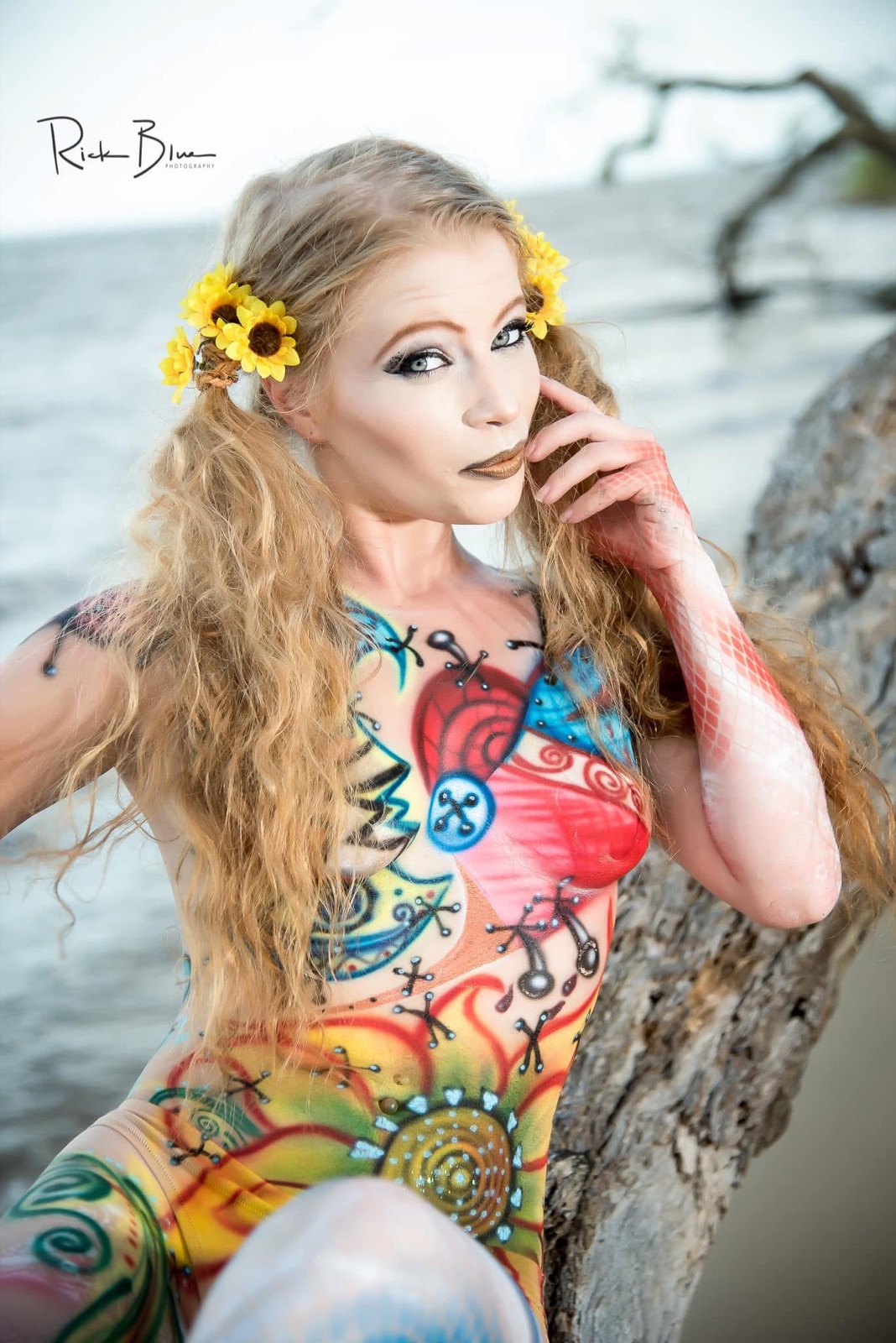 A model with floral body paint and flowers in her hair, by a tree