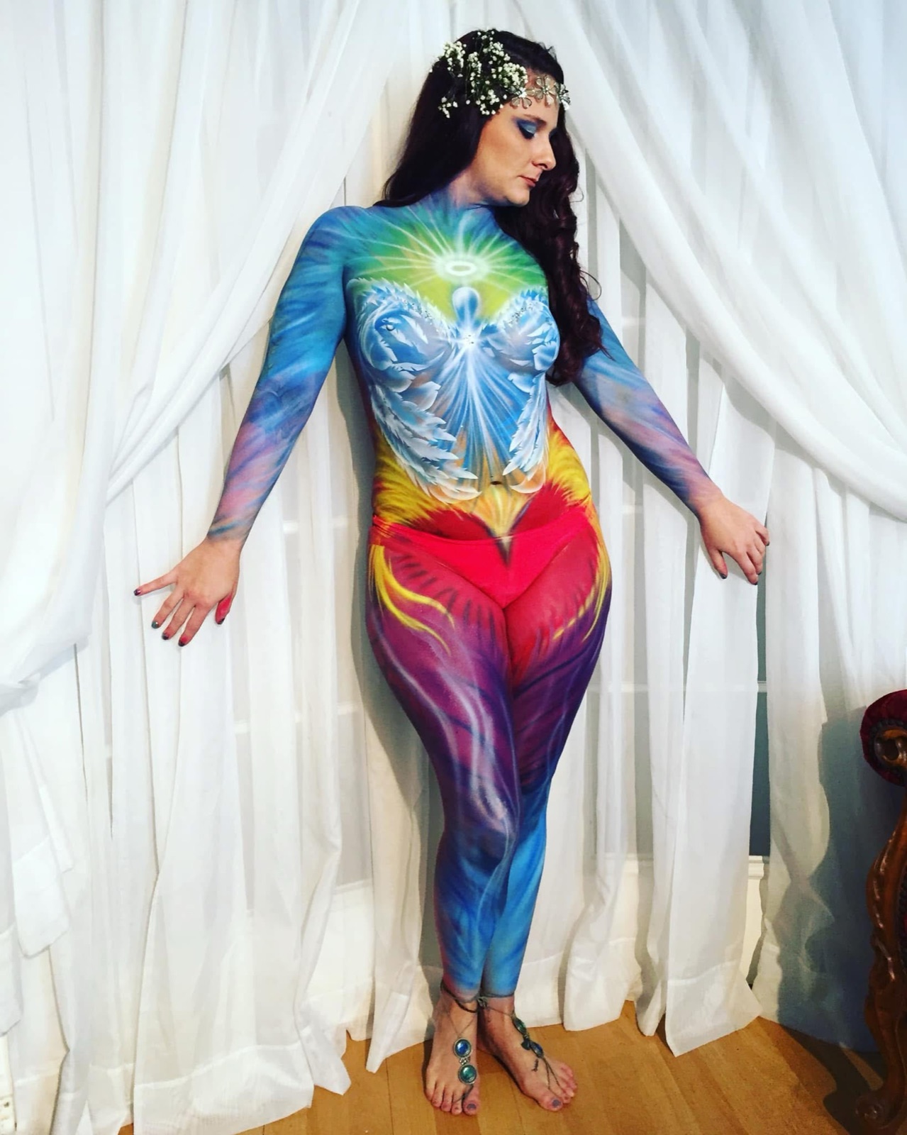 A figure painted head to toe in a flowing rainbow design against white