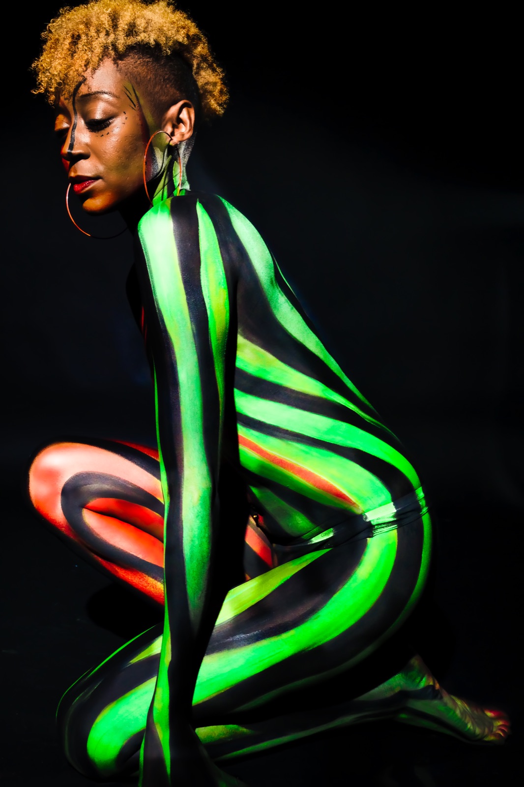A figure in electric green and orange striped UV body paint on black