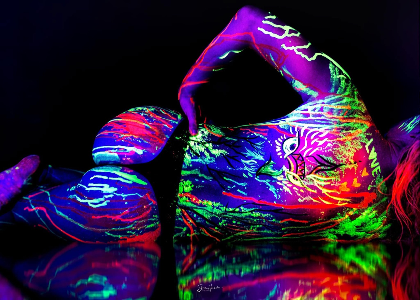 A torso covered in electric multicolour UV paint glowing on black