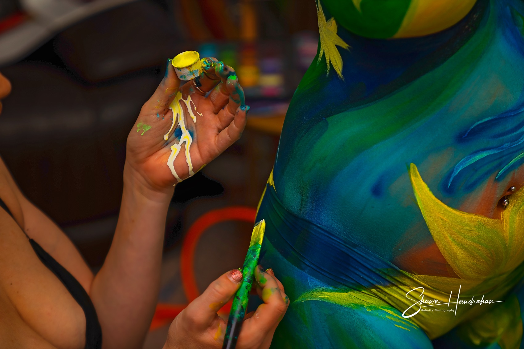 Tina's hands airbrushing a bright design onto skin, colour in progress