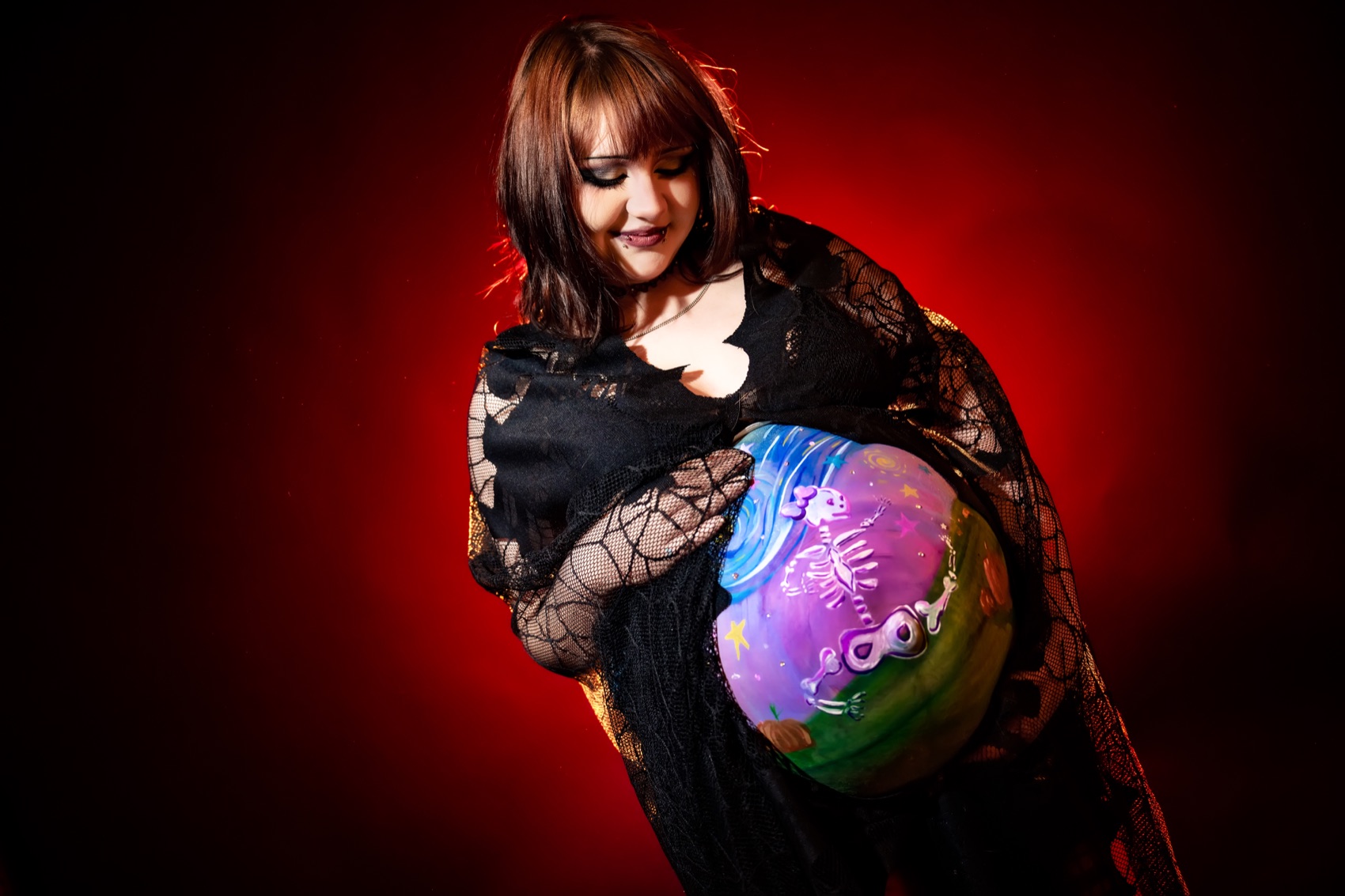 A figure in dramatic body paint cradling a hand-painted glowing sphere, lit against a deep red ground